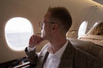 Pensativo hombre de negocios mirando por la ventana mientras viaja en jet privado - foto de stock