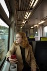 Rote Haare junge Frau schaut weg, während sie ihr Handy im Zug benutzt — Stockfoto