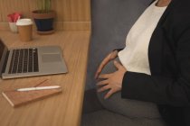 Grávida empresária tocando sua barriga na mesa no escritório — Fotografia de Stock