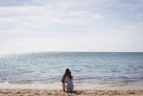 Visão traseira de mãe e filha na praia apontando e olhando para a vista — Fotografia de Stock