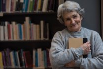 Porträt einer Seniorin, die ein Buch in der Bibliothek hält — Stockfoto