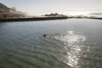 Femme nageant dans la piscine au bord de la plage en plein soleil — Photo de stock