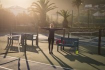 Jeune femme debout avec les bras tendus dans le court de tennis — Photo de stock