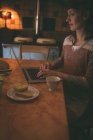 Mulher usando laptop enquanto toma café da manhã em casa — Fotografia de Stock
