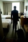 Vista trasera del hombre de negocios de pie con equipaje en la habitación de hotel - foto de stock
