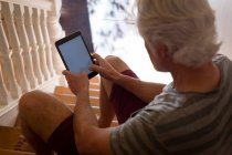 Старший мужчина использует цифровой планшет на лестнице дома — стоковое фото