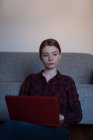 Jeune femme utilisant un ordinateur portable dans le salon à la maison — Photo de stock