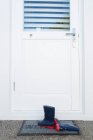 Botas Wellington em um tapete de porta na frente da porta da casa — Fotografia de Stock