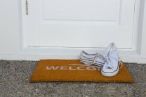 Primer plano de los zapatos de lona en una alfombra de la puerta - foto de stock
