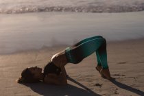 Mujer en forma realizando yoga en la playa al atardecer . - foto de stock