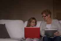 Бабуся і онука використовують ноутбук і цифровий планшет вдома — стокове фото