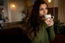Mujer pensativa tomando café en la sala de estar en casa - foto de stock