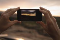 Жінка фотографує природу з мобільним телефоном на заході сонця — стокове фото