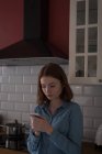 Молода жінка використовує мобільний телефон на кухні — стокове фото