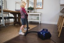 Boy using vacuum cleaner in living room at home — Stock Photo