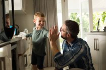 Father and son giving high five to each other in kitchen at home — Stock Photo