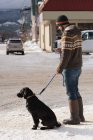 Mann mit Hund checkt Smartphone auf Gehweg in winterlicher Stadt. — Stockfoto