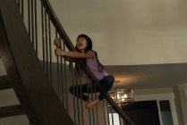 Chica feliz jugando en la barandilla escalera en casa - foto de stock
