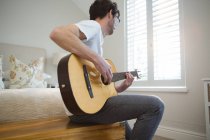Мужчина играет на гитаре в спальне дома — стоковое фото