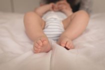 Primer plano del bebé en traje de bebé acostado en la cama en casa - foto de stock