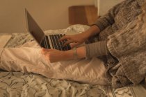 Средняя часть зрелой женщины, использующей ноутбук в спальне дома — стоковое фото