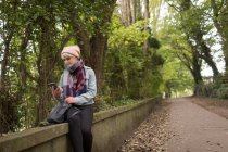 Giovane donna in abiti caldi utilizzando il suo telefono cellulare al parco — Foto stock