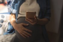 Sezione centrale della donna incinta che utilizza il telefono cellulare al caffè — Foto stock