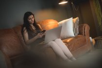 Frau mit Laptop benutzt Handy zu Hause — Stockfoto