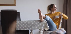 Femme réfléchie avec les pieds en l'air prendre un café à la maison — Photo de stock