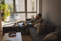 Пара с помощью ноутбука и мобильного телефона в гостиной на дому — стоковое фото