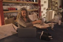 Жіночий гончар дивиться на ноутбук під час формування глини вдома — стокове фото
