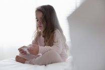 Маленька дівчинка використовує мобільний телефон у спальні вдома — стокове фото