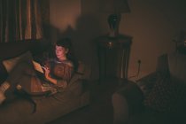 Mujer usando tableta digital en el sofá en la sala de estar en casa - foto de stock