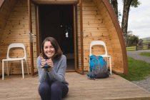 Portrait of happy woman having coffee outside the log cabin — Stock Photo