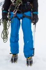 Male mountaineer standing with rope and ice axe on a snowy region during winter — Stock Photo