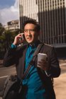 Chinese businessman with cup of coffee talking on mobile phone in city street — Stock Photo