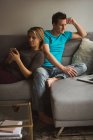 Casal usando telefone celular e laptop na sala de estar em casa — Fotografia de Stock