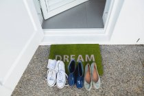 Varie scarpe tenute su un tappetino davanti alla porta di casa — Foto stock