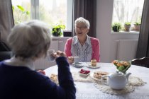 Amigos mayores interactúan bruja entre sí mientras toman café en casa - foto de stock