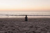 Vista posteriore della donna seduta sulla spiaggia sabbiosa al tramonto . — Foto stock