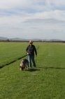 Frau geht an einem sonnigen Tag mit Schäferhund auf dem Feld spazieren — Stockfoto