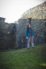 Jovem caminhante do sexo masculino em pé em ruínas antigas no campo — Fotografia de Stock