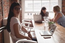Weibliche Führungskraft blickt in die Kamera und Kollegen diskutieren im Hintergrund im Büro — Stockfoto