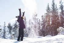 Mujer lanzando nieve en el aire en un bosque invernal . - foto de stock
