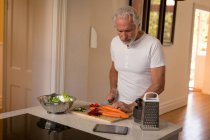 Uomo anziano che taglia verdure in cucina a casa — Foto stock