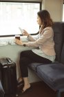 Esecutivo femminile che utilizza il cellulare mentre prende il caffè in treno — Foto stock
