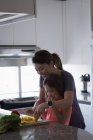 Mãe e filha cortando legumes na cozinha em casa — Fotografia de Stock