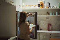 Frau benutzt digitales Tablet beim Öffnen eines Kühlschranks zu Hause — Stockfoto