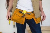 Sección media del carpintero masculino con cinturón de herramientas en el taller - foto de stock