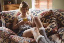Mulher usando telefone celular no sofá na sala de estar em casa — Fotografia de Stock
